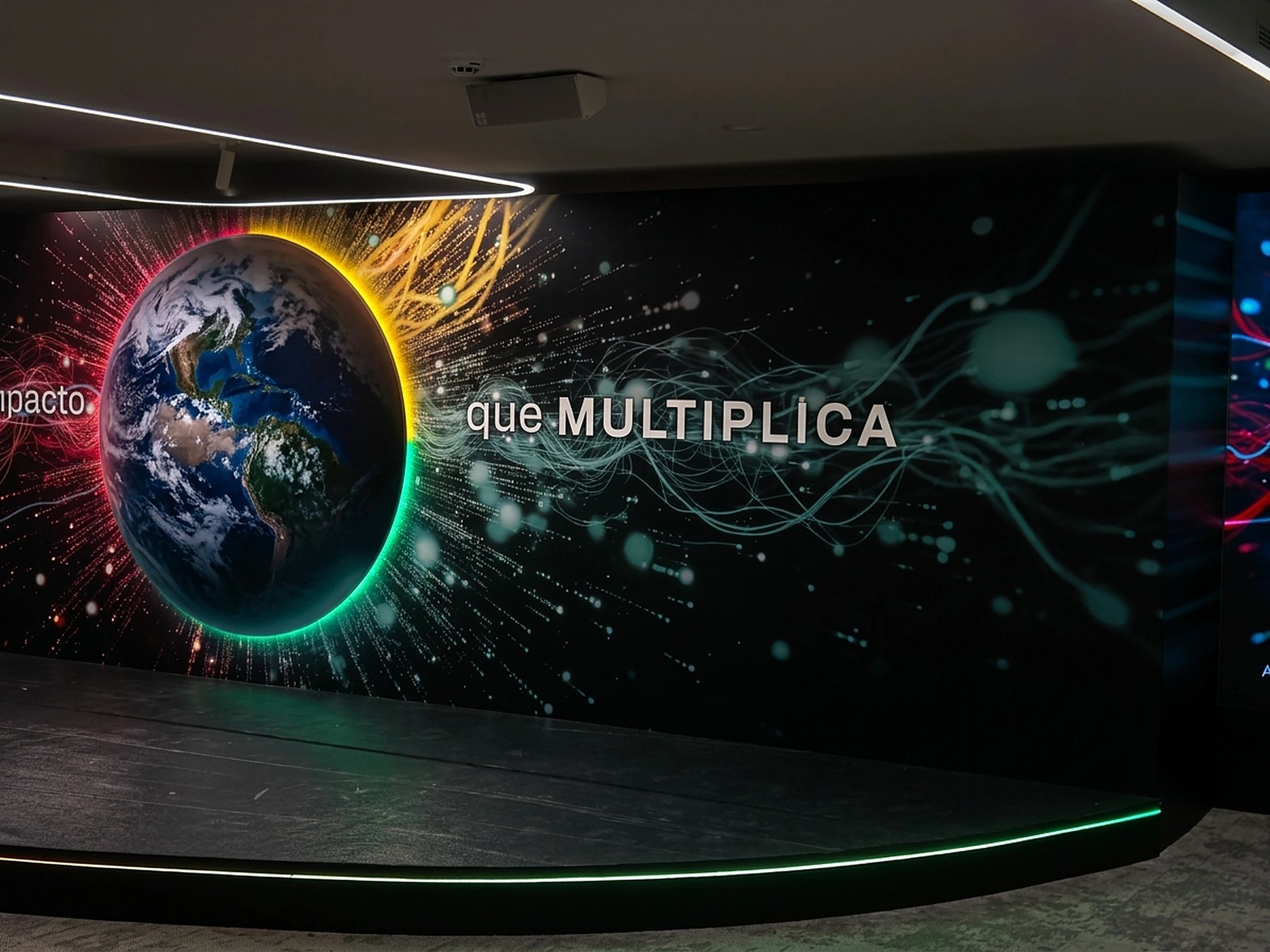 Mural impreso «Impacto que multiplica» con la Tierra iluminada en un escenario corporativo
